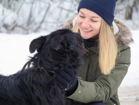 Young woman playing with funny Black pet dog with snow. on the background. Playing with the snow. Adorable dog enjoying her time, winter time. Copy spaceの写真素材