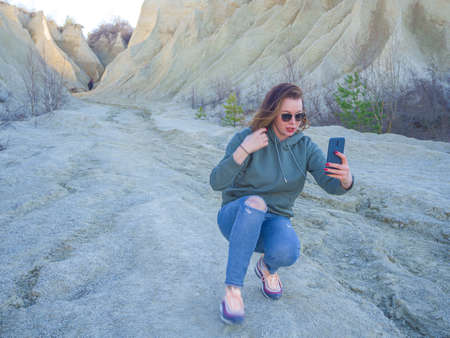Hiker on mountain top with smartphone. Woman is standing and taking a picture on smartphone. Abandoned Quarry Of Rummu, Estonia. Scenic View Of Land Against Clear Blue Sky. Panoramic View.の写真素材