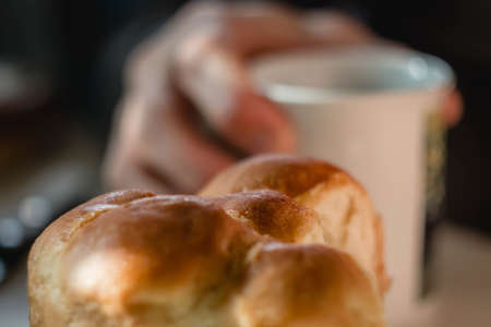 Chocolate croissants, bun and cakes, cup of fruit tea on white wooden table. man hands making tea, stirring slowly with spoon. delicious nourishing breakfastの写真素材