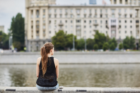 A young girl sitting on the banks of the Moscow river back. summer in Moscowの写真素材