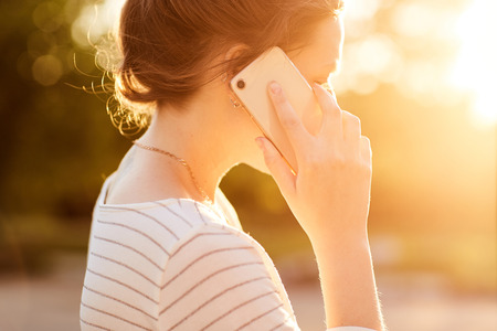young girl talking on the phone in the summer in the Park at sunsetの写真素材