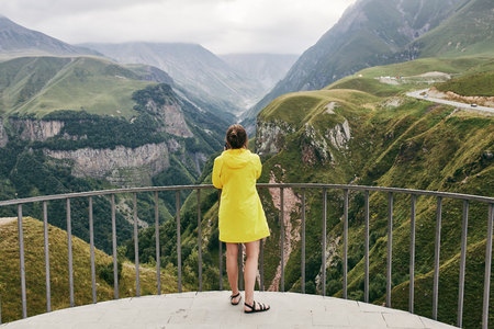 A young Girl in a yellow raincoat tourist photographs the mountains. Girl making a photo shoot of...