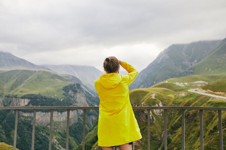 A young Girl in a yellow raincoat tourist photographs the mountains. Girl making a photo shoot of...