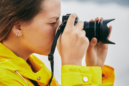 A young Girl in a yellow raincoat tourist photographs the mountains. . Girl making a photo shoot of mountain. Georgia. Summer. August. Mount Kazbegi.の写真素材