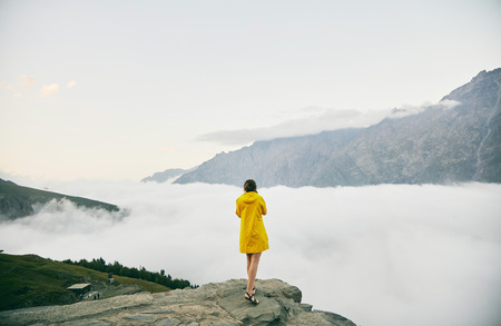A young Girl in a yellow raincoat tourist photographs the mountains. . Girl making a photo shoot of...