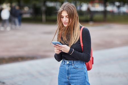 A young Russian girl is typing a message on the phone. Moscow. Autumn. A girl writes SMS message. Communicates in social networksの写真素材