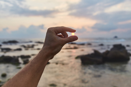 The guy holds the sunset sun in his hands. Indian ocean.の写真素材