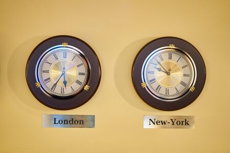 A wall clock showing the time difference between London and New York. Time zones on a watch.の写真素材