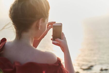 Young girl takes pictures of landscapes on the phone. The Girl photographs the sunset on the phone. ...