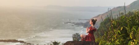 A young girl practices yoga in a red dress on a mountain in India. Banner. Text copy. Text field.の写真素材