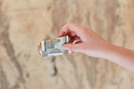 A girl holds a rolled-up bill of 500 Indian rupees in her hand.の写真素材