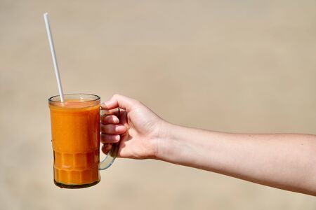 A girl holds a glass with freshly squeezed papaya juice. Hand close-up.