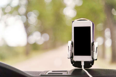 Mobile phone with GPS card in the car. A white smartphone on a stand in the car is used for...