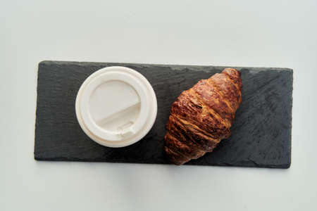 Red cup with coffee and a croissant on a table in a cafe.の写真素材