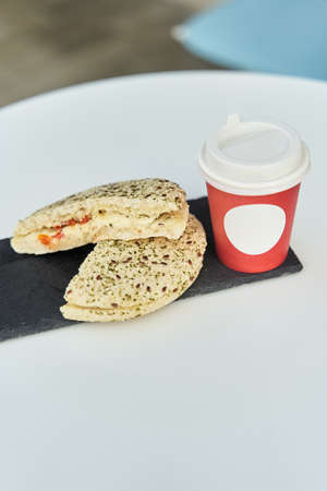 A sandwich with a red plastic glass of coffee on the table in a coffee shop.