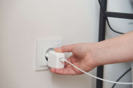 A young girl inserts a plug into an outlet. Young woman plugs the phone charger into the socket.
