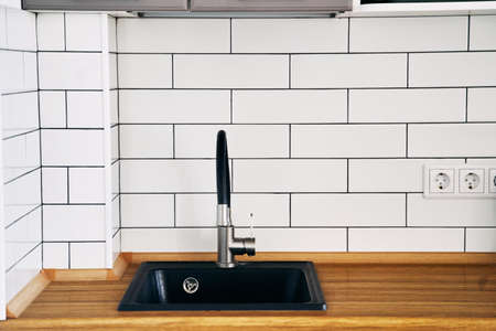 Stylish black sink and faucet on a wooden countertop in a kitchen set close-upの写真素材