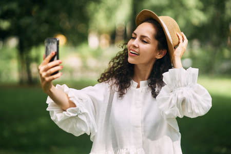 Young beautiful girl in a hat makes a selfie on her phone in the parkの写真素材