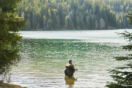 Fisher man stands in the water and catch fish in the lake on a background of mountains