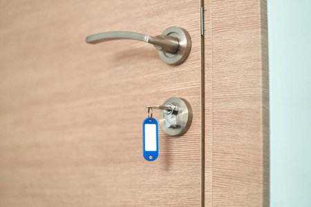 A key with a blank keychain in the lock of a wooden door close upの写真素材