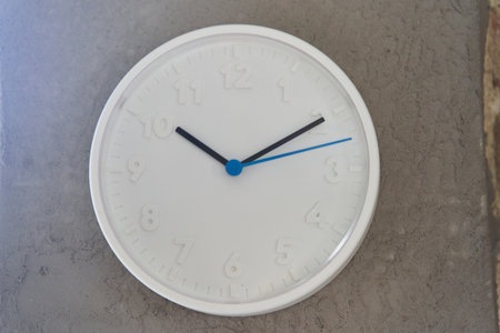 White big wall clock with blue second hand on rough cement wall