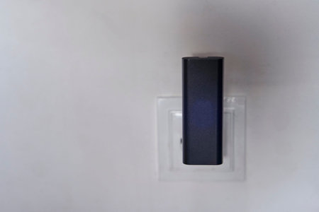A black wi-fi router is connected to a white outlet on a white wall