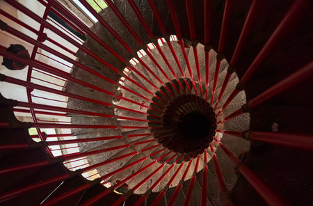 Top view of steep spiral staircase with red handrails