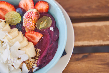 Smoothie bowl with fresh fruit, berries and muesli on the background of a wooden table. Healthy vegetarian breakfastの写真素材