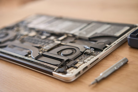 Disassembled laptop alongside various tools placed neatly on a wooden surface for repairsの写真素材