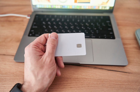 Person holds credit card in front of computer for online transaction