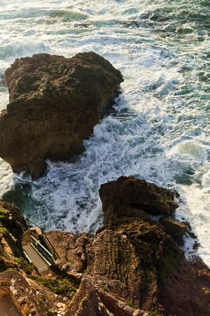 The Ocean Waves Powerfully Crash Against the Rocky Shoreline as the Sun Sets Beautifullyの写真素材