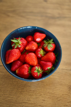 A Charming Bowl Full of Fresh and Ripe Strawberries Placed on a Rustic Wooden Tableの写真素材