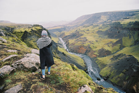 The back of a girl standing and looking at a mountain river in Iceland. Grainy film in the style of old photosの写真素材