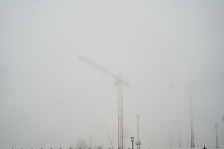 A construction crane stands out in a foggy landscape, enhancing the industrial sceneryの写真素材
