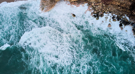 Aerial view of ocean waves crashing on rocks in Nazare, Portugal