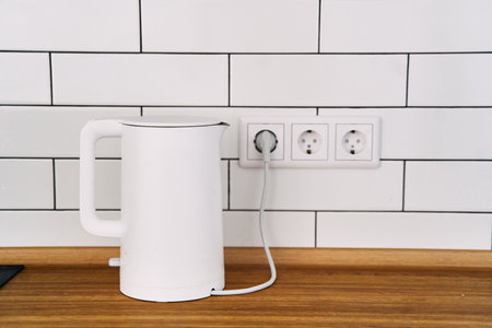 White stylish electric kettle stands on a wooden kitchen countertopの写真素材