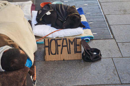 Milan, Italy February 2023: Poor homeless boy sleeping in the street in the sleeping bag with his dogのeditorial素材