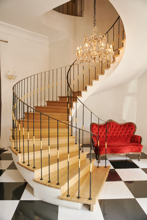 Hall with spiral staircase, glass chandelier and red sofa downstairs