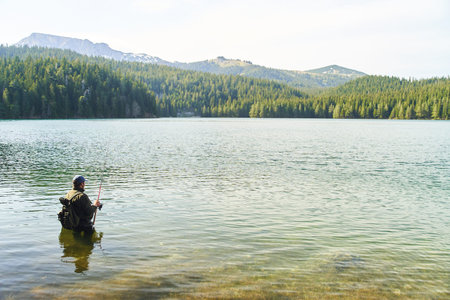 Fisher man stands in the water and catch fish in the lake on a background of mountains