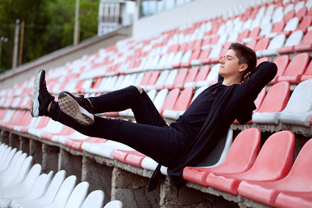Guy in dark clothes sits contentedly at an empty stadiumの写真素材