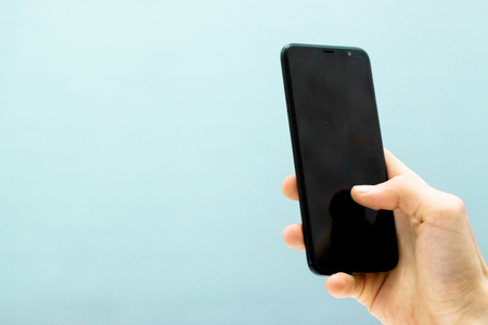 Hand holding smartphone mobile and touching screen isolated on blue backgroundの写真素材