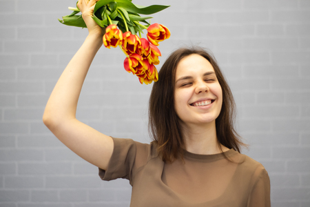 Beautiful girl in the brown dress with flowers tulips in hands on a light background.の写真素材