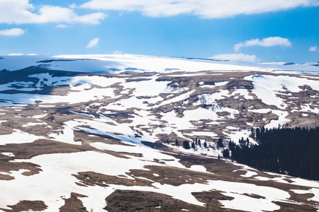 Lago Naki spring plateau with snowy hills, blue sky and clouds.