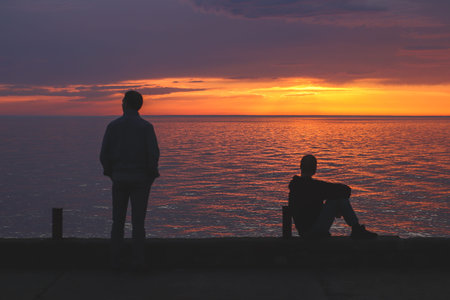 Silhouettes of 2 people looking at the sunset on the embankment of the Black Sea coast in Kobuleti,...