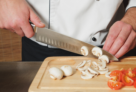 chef cutting mushrooms and tomats on table with knifeの写真素材