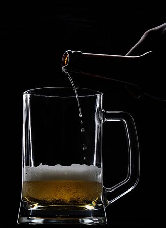 beer come from bottle in empty glass on blackの写真素材