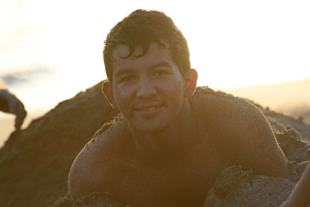 happy guy teenager buried in sand light of sunの写真素材