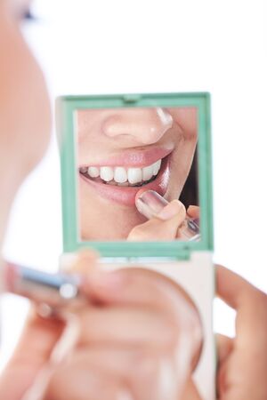 woman smiling putting lipstick on reflection of mirrorの写真素材