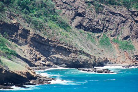 ocean waves hitting big stone rocks on sunny dayの写真素材
