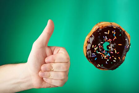 Thumb up to sweet chocolate donut  isoaletd on greenの写真素材